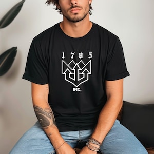 May include: Black t-shirt with a white graphic design. The design includes the numbers "1785" above a stylized emblem and the word "INC." below. The shirt has short sleeves and a crew neck.