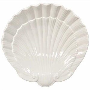 May include: A white ceramic serving dish shaped like a large scallop shell. The dish features a glossy finish with deep, radiating ridges that extend from the base to the scalloped edges, creating a textured, fan-like appearance.