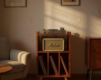 May include: A wooden record player stand with a turntable on top and a Marshall speaker in the middle. The stand has several compartments for storing vinyl records. The speaker is tan with the Marshall logo. The stand is in a room with artwork.
