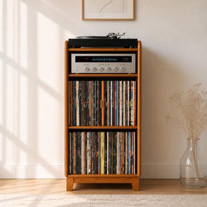 Peut inclure: Un meuble de rangement en bois brun clair à trois étagères. L'étagère supérieure supporte une platine vinyle noire et un amplificateur argenté. Les étagères du milieu et du bas contiennent des rangées de disques vinyles verticaux.