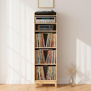 Könnte beinhalten: Ein hohes Regal aus hellem Holz mit vier Ebenen. Auf der obersten Ablage stehen ein schwarzer Plattenspieler und ein silberner Receiver. Die drei unteren Fächer sind mit Reihen von Vinyl-Schallplatten in bunten Hüllen gefüllt.