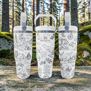 Può includere: Tre bicchieri bianchi Stanley con manico e una stampa a linee nere raffigurante scene all'aperto, tra cui escursionisti, una tenda, un cervo, una bussola, binocoli e un cartello con il testo EXPLORE, DISCOVER e ADVENTURE stampato sopra.