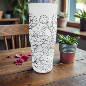 May include: A white insulated travel mug with a black floral peony design. The mug is cylindrical and has a silver rim. It rests on a wooden table with scattered pink flower petals.