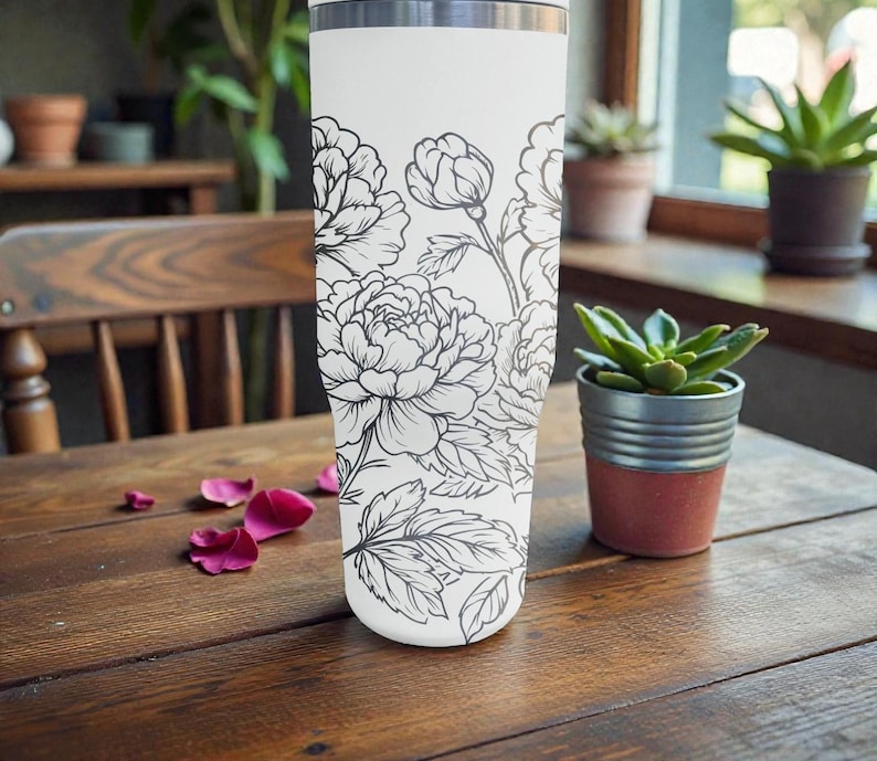 May include: A white insulated travel mug with a black floral peony design. The mug is cylindrical and has a silver rim. It rests on a wooden table with scattered pink flower petals.