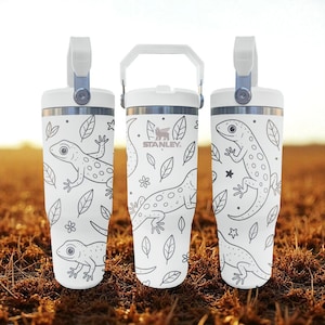 May include: Three white insulated tumblers with a handle and a lizard and leaf design. The tumblers have a silver rim and a white handle. The design includes a lizard, leaves, and flowers. The Stanley logo is visible on one of the tumblers.