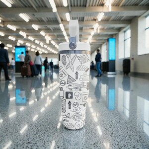 Puede incluir: Un termo de viaje blanco con asa y tapa plateadas. El termo est&aacute; decorado con dibujos lineales negros de aviones, pasaportes y equipaje. La fecha "30-01-2018 DEPARTED" est&aacute; impresa en el termo.