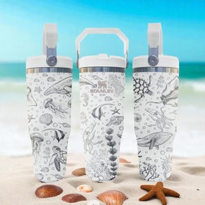 May include: Three white insulated tumblers with a handle and a lid. Each tumbler features a black and white ocean-themed illustration of marine life, including whales, jellyfish, and sea turtles. The Stanley logo is visible on one of the tumblers.