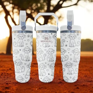 May include: Three white insulated tumblers with a monkey pattern and a handle. The tumblers have a white lid and handle. The monkey pattern is in black and white. The Stanley logo is visible on the center tumbler.