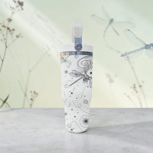 May include: White insulated tumbler with a handle and a black dragonfly design. The tumbler features a screw-on lid and a handle. The design includes dragonflies, stars, and celestial elements.