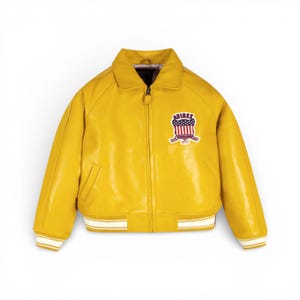 May include: A bright yellow leather jacket with a zip-up front and a classic collar. The jacket features a patch on the chest with a red, white, and blue emblem and the word "AVIREX". The cuffs and hem have white and yellow striped detailing.