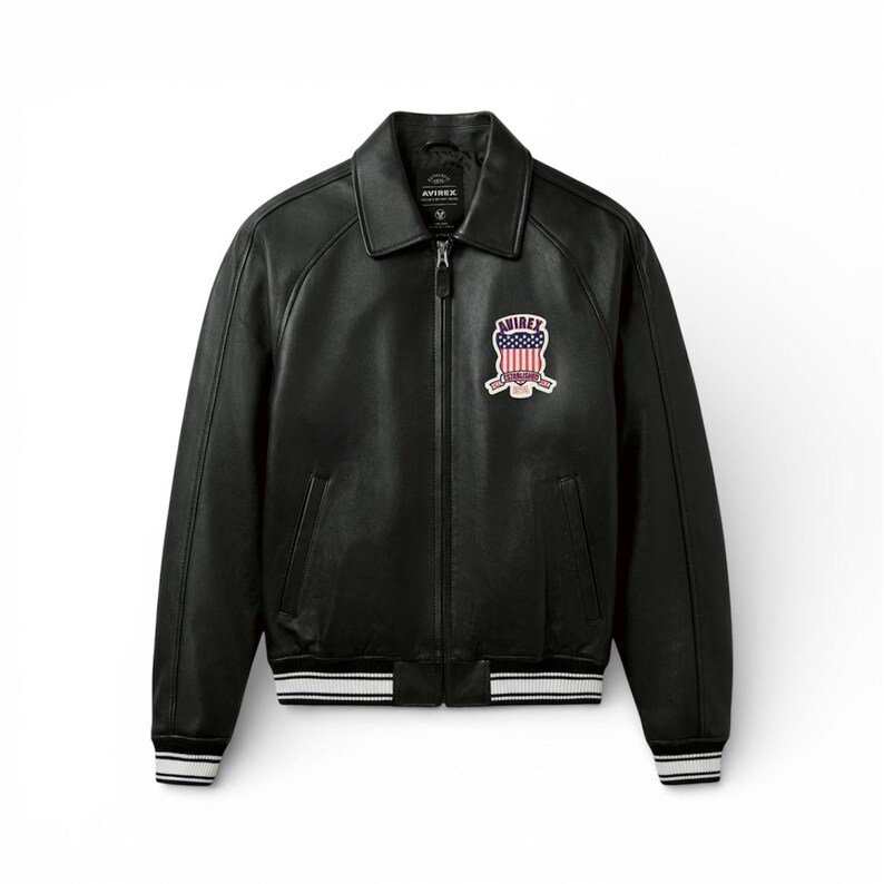 May include: Black leather jacket with a zip-up front, collar, and a patch on the chest. The patch features a design with red, white, and blue colors. The jacket has white stripes on the cuffs and waist. The brand name "AVIREX" is visible.