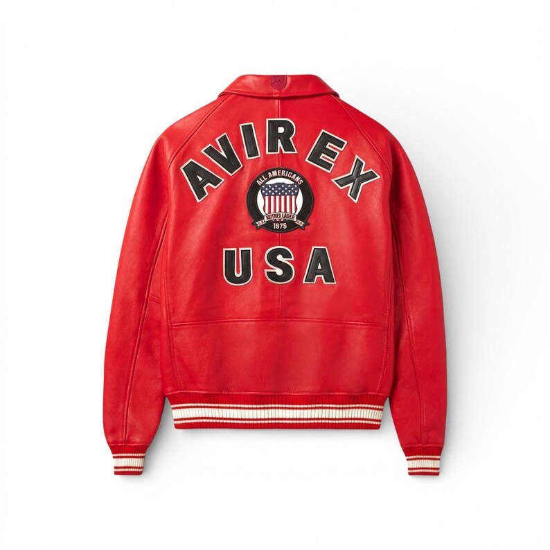 May include: A vibrant red leather jacket with the word "AVIREX" arched across the shoulders. Below, the word "USA" is prominently displayed. The jacket features a circular patch with an American flag design and the text "ALL AMERICANS" and "1975". White and red striped cuffs and hem complete the design.