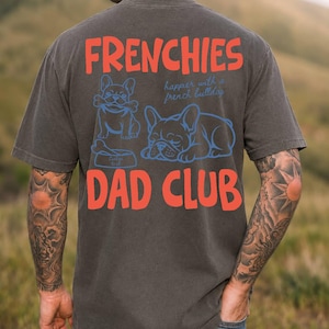 May include: Dark gray t-shirt with the words "FRENCHIES DAD CLUB" in red block letters. The shirt features blue illustrations of French Bulldogs, one with a bone and the other sleeping. The text "happier with a french bulldog" is also included.