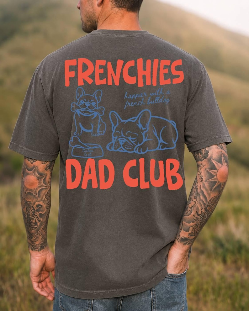 May include: Dark gray t-shirt with the words "FRENCHIES DAD CLUB" in red block letters. The shirt features blue illustrations of French Bulldogs, one with a bone and the other sleeping. The text "happier with a french bulldog" is also included.