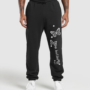 May include: Black sweatpants with a drawstring waist and white graphic of two butterflies, stars, and the text "the butterfly". The sweatpants are paired with white sneakers.