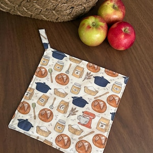 May include: A square fabric potholder featuring a repeating pattern of baking-themed illustrations including sourdough loaves, blue Dutch ovens, jars labeled Day 7, flour bags, whisks, and a red stand mixer on a cream-colored background.