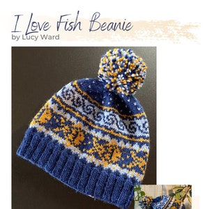 May include: A blue and yellow knitted beanie with a white pom pom. The beanie has a pattern of fish and waves. The text "I Love Fish Beanie" is written above the beanie. The text "by Lucy Ward" is written below the beanie.