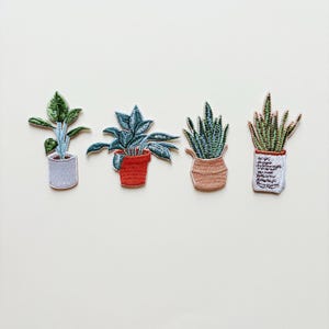 Può includere: Quattro toppe ricamate di piante. Le toppe raffigurano varie piante in vaso con foglie e steli verdi e verde-blu. I vasi sono in tonalità di rosso, beige e grigio. Le toppe sono su sfondo bianco.