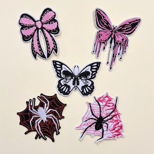May include: Embroidered patches featuring a pink bow, two butterflies, and two spiders. One butterfly has a skull design, and another has a dripping effect. The spiders are on webs, one red and one pink.
