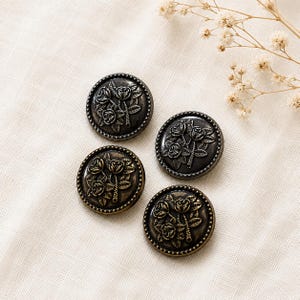 May include: Four round metal buttons featuring a raised relief design of three roses with leaves. Each button has a dark bronze finish with a beaded border edge. The buttons are arranged in a square formation, showcasing detailed floral engravings.