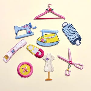 May include: A collection of nine embroidered sewing-themed patches including a pink hanger, a blue sewing machine, a yellow iron, a blue spool of thread, a white measuring tape, a pink safety pin, a pink button, a dress form, and pink scissors.