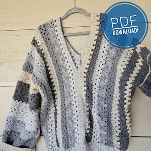 May include: A crocheted sweater with a V-neck and long sleeves. The sweater is made in a striped pattern of gray, white, and light blue yarn. The sweater is hanging on a hanger. The text "PDF DOWNLOAD!" is visible in the upper right corner of the image.