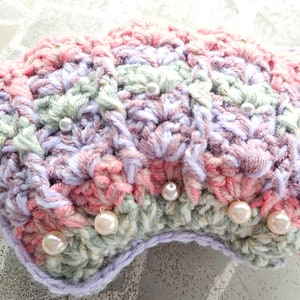 May include: A crocheted headband with a scalloped edge, featuring a pastel color scheme of pink, purple, and green. The headband is adorned with white pearl beads.