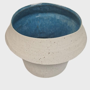 May include: A ceramic bowl with a wide, speckled, off-white rim and a deep blue interior. The bowl has a rounded shape and a pedestal base. The exterior has a textured, speckled finish. This decorative bowl is suitable for home decor. The bowl's diameter is approximately 20 cm.