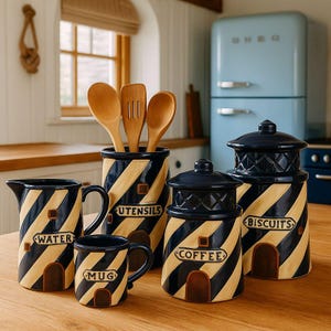 May include: A set of navy and beige striped ceramic kitchen items. Includes a water jug, mug, utensil holder with wooden spoons, and canisters labelled "coffee" and "biscuits". The lighthouse design gives a nautical feel.
