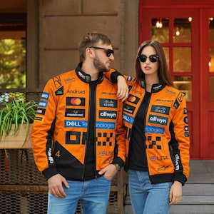 Può includere: Giacche arancioni e nere in stile racing con loghi di sponsor, tra cui "Android", "McLaren" e "Hilton". Le giacche hanno colletto, polsini e orlo neri, con il numero "4" sul davanti. Le giacche sono indossate con jeans blu.