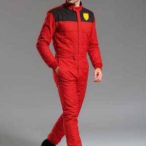 May include: Red racing suit with black shoulder accents and a yellow emblem. The one-piece suit has a quilted design, a stand-up collar, and a belt at the waist. The model is wearing black shoes.