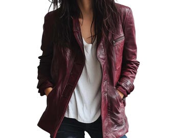 May include: A burgundy leather jacket with a classic design. The jacket features a notched collar, a front zipper pocket, and button closures. The model is wearing a white top and blue jeans.