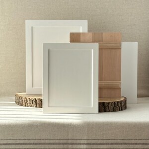 Pu&ograve; includere: Un assortimento di campioni di ante per armadi in vari stili e finiture. L'immagine presenta due ante bianche, una porta in legno naturale e un pannello trasparente. Le ante sono esposte su una fetta di legno, mostrando le diverse trame e i design.
