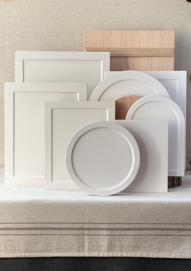 May include: A collection of off-white, geometric wooden shapes, including rectangles, squares, and circles. Some pieces have raised edges, and a wooden box is visible in the background. The items are arranged on a neutral-toned surface.
