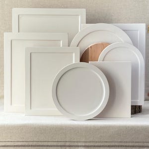 Pu&ograve; includere: Una collezione di vassoi da portata e oggetti decorativi bianchi dalle varie forme geometriche. I design includono rettangolari, quadrati, circolari e ad arco. I pezzi sono disposti su una superficie dai toni neutri, mostrando una variet&agrave; di dimensioni e forme.