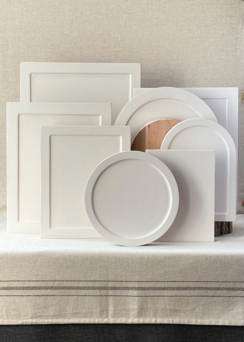Pu&ograve; includere: Una collezione di vassoi da portata e oggetti decorativi bianchi dalle varie forme geometriche. I design includono rettangolari, quadrati, circolari e ad arco. I pezzi sono disposti su una superficie dai toni neutri, mostrando una variet&agrave; di dimensioni e forme.