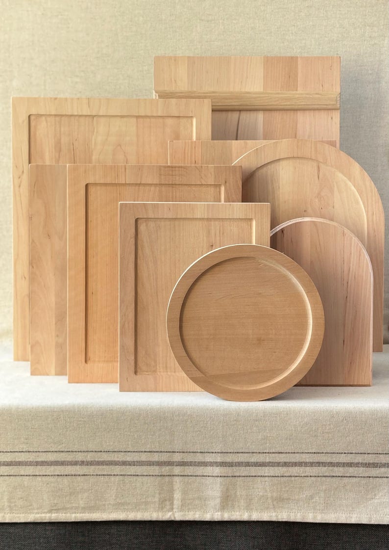 May include: A selection of wooden chopping boards and serving platters in various shapes. The items are crafted from light-coloured wood and include rectangular, square, and circular designs. Some have raised edges or decorative features.
