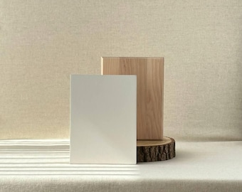 May include: A minimalist product display featuring a white rectangular block and a natural wood block, both standing upright. The wood block rests on a tree slice. The backdrop is a neutral beige fabric, creating a clean, modern aesthetic.