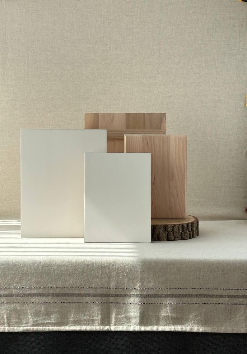 May include: A studio shot featuring a collection of blank canvases and wooden blocks. Two white rectangular canvases stand in front of two wooden blocks and a wood slice. The canvases are different sizes. The background is a neutral beige.
