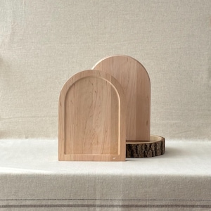 May include: Two wooden arched cutting boards of different sizes. The boards are made of light-coloured wood with a natural grain pattern. One board is in front of the other, with the larger board resting on a wooden slice.