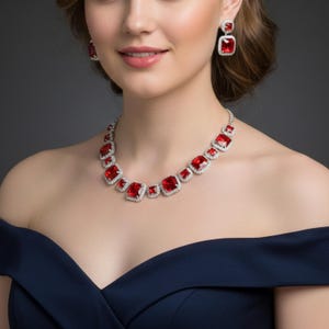 May include: A red and silver jewelry set featuring a necklace and matching earrings. The necklace and earrings have square red gemstones surrounded by a silver setting. The woman in the image is wearing a dark blue dress.