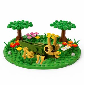May include: A toy block grasshopper in green and tan sits on a green circular base with flowers and trees. The scene includes red, yellow, pink, and white flowers, and two green trees with brown trunks.