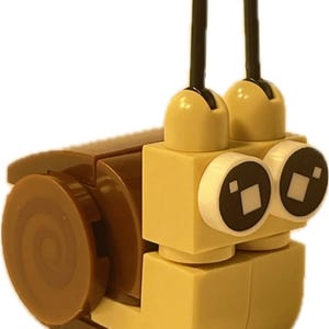 May include: A whimsical snail figure constructed from interlocking toy bricks. The snail features a brown shell, a tan body, and two dark brown antennae with rounded tips. The eyes are white with black square pupils. A fun, creative toy.