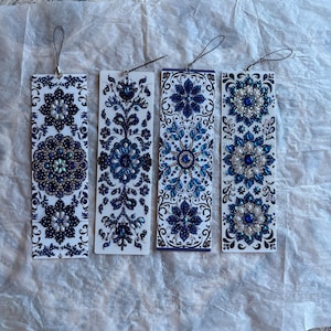 Op de afbeelding: Vier decoratieve bladwijzers met ingewikkelde blauw-witte bloemmotieven. Elke bladwijzer heeft een ander patroon, versierd met kralen en imitatieparels. Ze hebben zwarte lussen om op te hangen.