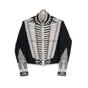 May include: Black cropped jacket with white and silver embroidery. The jacket features a high collar, silver button details, and ornate white embroidery on the sleeves and shoulders. A formal garment.