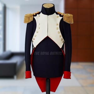 Puede incluir: Chaqueta de uniforme militar azul marino con chaleco blanco, charreteras doradas y detalles rojos. La chaqueta tiene botones dorados y puños rojos. El texto "THE ROYAL OUTFITS" es visible. El uniforme se exhibe en un maniquí.
