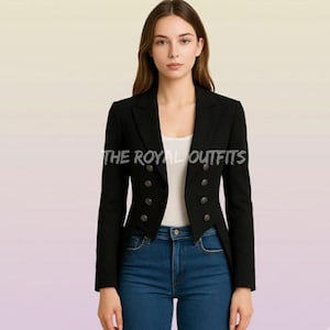 Op de afbeelding: Een zwarte blazer met een dubbele rij knopen en een getailleerde pasvorm. De blazer heeft een revers en wordt gedragen met een blauwe jeans. De tekst "THE ROYAL OUTFITS" is zichtbaar.
