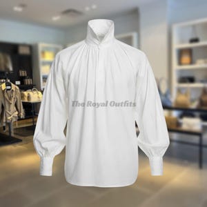 May include: A white long-sleeve shirt with a high collar and gathered detailing. The shirt features a button closure at the neck and voluminous sleeves that taper to buttoned cuffs. The text "The Royal Outfits" is visible on the shirt.