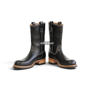 May include: A pair of black leather mid-calf boots featuring a rounded toe, pull-on tabs at the top, and light-colored stacked wooden heels with black outsoles. The boots have visible light-colored stitching and the text Velikor Supply.