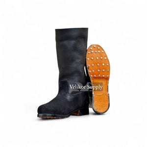 Puede incluir: Botas de cuero negro con empeine de ante en contraste. Una bota está de pie, la otra muestra la suela tachonada. Las botas tienen una caña alta y un tacón resistente. Botas militares o de trabajo.